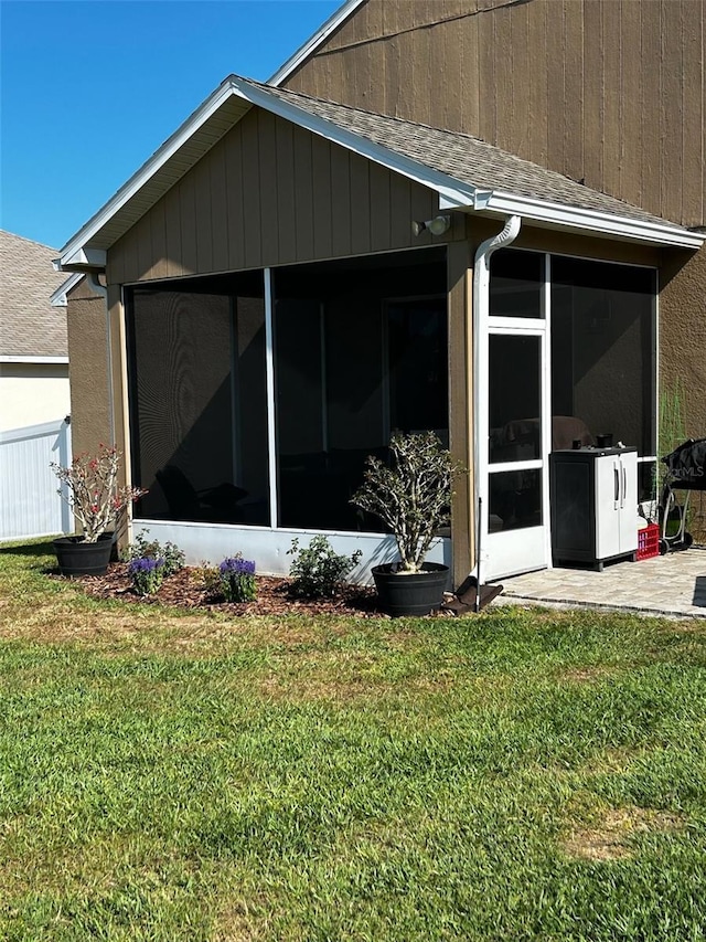view of side of property with a sunroom, roof with shingles, and a yard