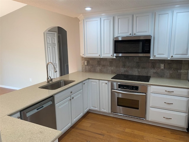 kitchen with appliances with stainless steel finishes, a sink, arched walkways, tasteful backsplash, and recessed lighting
