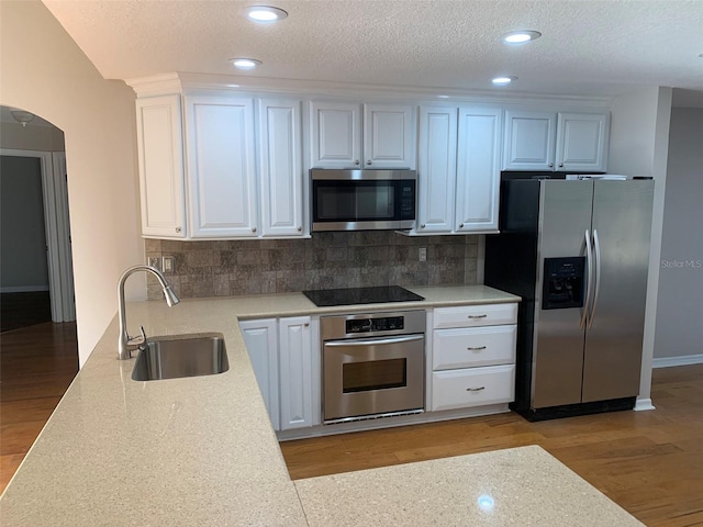 kitchen with appliances with stainless steel finishes, a sink, light wood-type flooring, light countertops, and backsplash