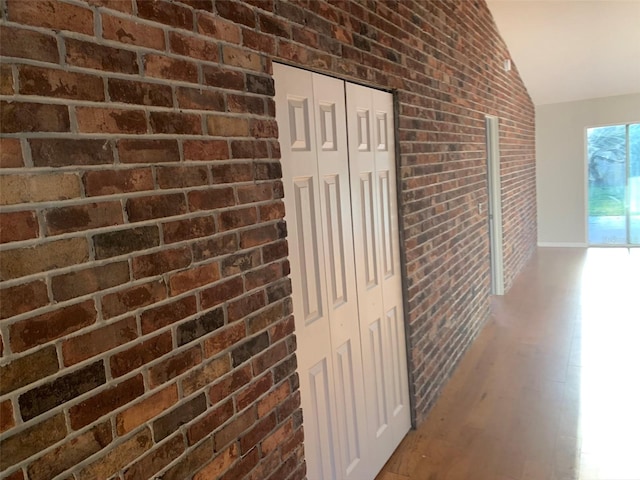 corridor with brick wall, wood finished floors, and lofted ceiling