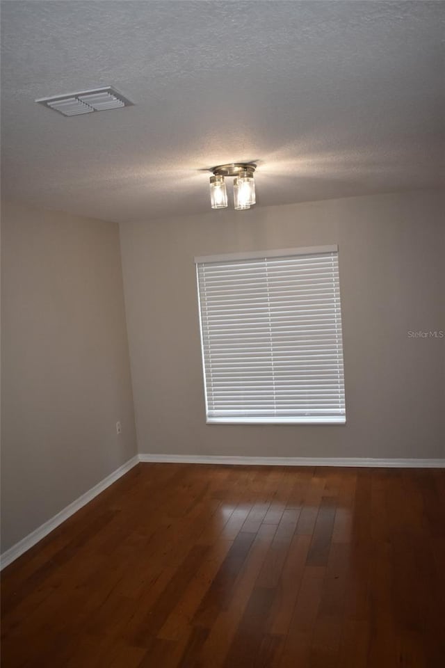 unfurnished room featuring baseboards, wood finished floors, and a textured ceiling