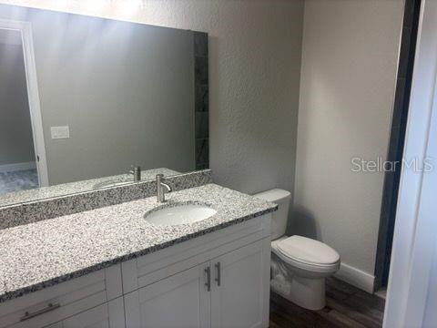 bathroom featuring toilet, a textured wall, wood finished floors, baseboards, and vanity