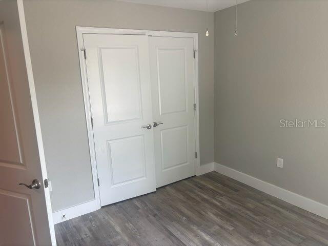 unfurnished bedroom featuring baseboards, wood finished floors, and a closet