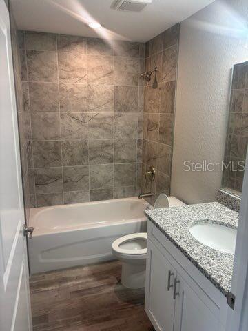 bathroom featuring wood finished floors, bathtub / shower combination, toilet, vanity, and a textured wall