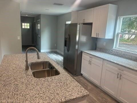 kitchen featuring a sink, white cabinets, black fridge with ice dispenser, light stone countertops, and wood finished floors