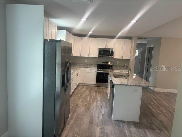 kitchen with stainless steel appliances, a sink, wood finished floors, light stone countertops, and white cabinetry