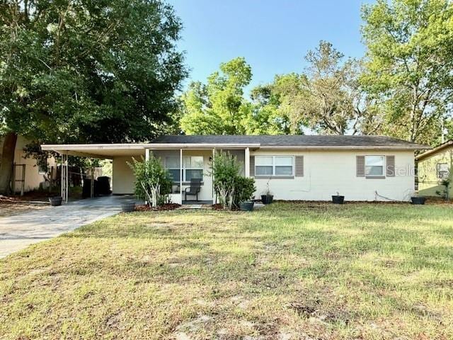 ranch-style house featuring driveway, an attached carport, and a front lawn