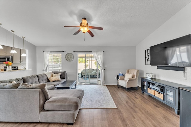 living area featuring a ceiling fan, wood finished floors, lofted ceiling, baseboards, and a textured ceiling