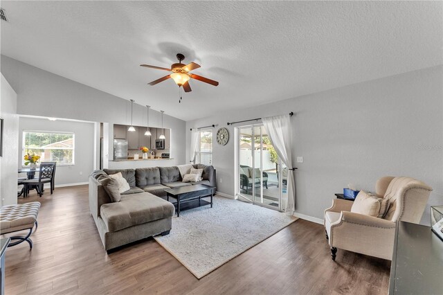 living area with wood finished floors, ceiling fan, vaulted ceiling, baseboards, and a textured ceiling