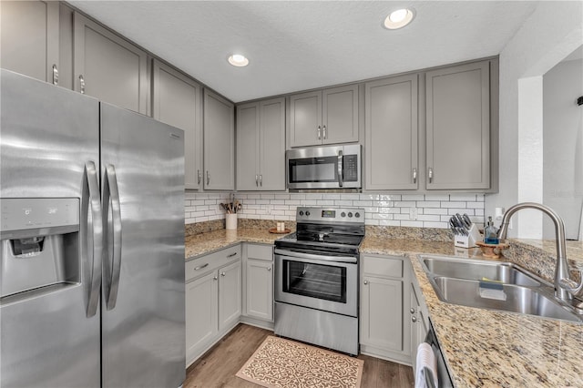 kitchen featuring appliances with stainless steel finishes, a sink, gray cabinets, light wood-style floors, and decorative backsplash