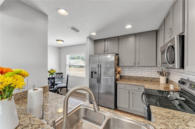 kitchen with stainless steel appliances, gray cabinetry, a sink, a textured ceiling, and decorative backsplash