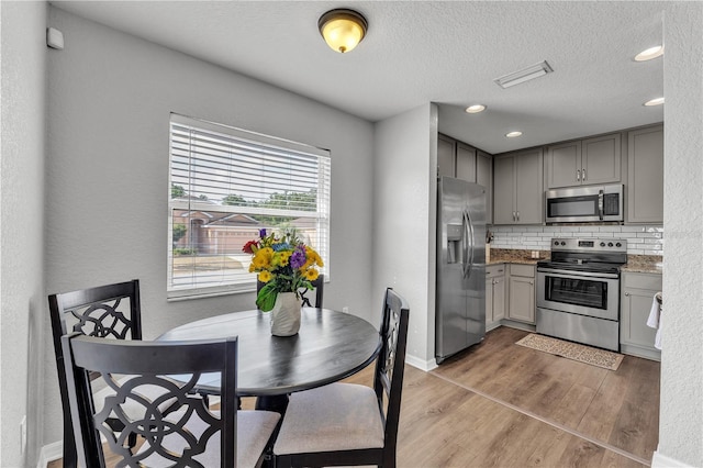 kitchen with appliances with stainless steel finishes, gray cabinets, light wood-type flooring, tasteful backsplash, and a textured ceiling