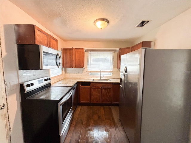 kitchen featuring stainless steel appliances, dark wood-type flooring, a sink, brown cabinets, and tasteful backsplash