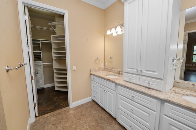 full bath with double vanity, crown molding, a spacious closet, and baseboards