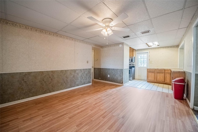 spare room with light wood-style flooring, wainscoting, a paneled ceiling, a ceiling fan, and baseboards