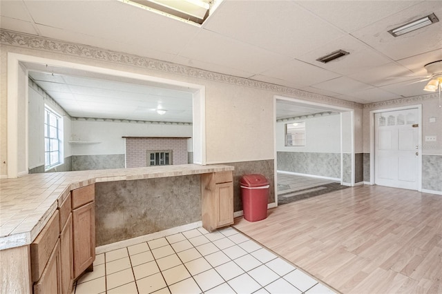 kitchen with tile counters, wainscoting, a drop ceiling, light wood finished floors, and a fireplace