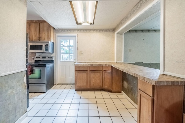 kitchen featuring stainless steel appliances, brown cabinets, light tile patterned floors, light countertops, and a textured wall