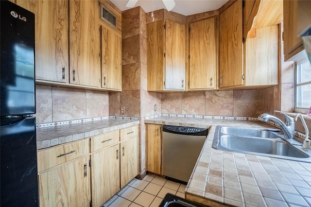 kitchen featuring freestanding refrigerator, stainless steel dishwasher, tile countertops, a sink, and decorative backsplash