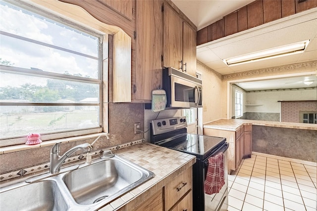 kitchen with stainless steel appliances, a sink, light tile patterned flooring, and brown cabinetry