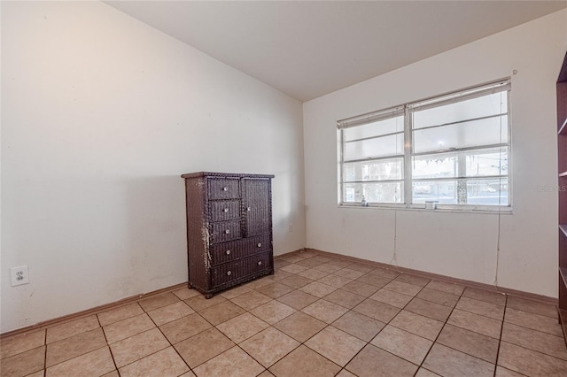 spare room featuring lofted ceiling and light tile patterned floors