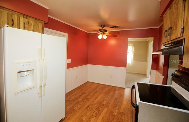kitchen with white appliances, under cabinet range hood, ceiling fan, brown cabinetry, and wainscoting