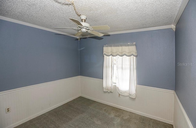 spare room with wainscoting, a ceiling fan, a textured ceiling, crown molding, and carpet