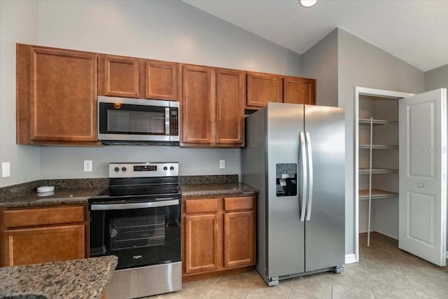 12654 Belcroft Dr, Riverview, FL 33579 - kitchen featuring stainless steel appliances, vaulted ceiling, brown cabinetry, light tile patterned floors, and dark stone countertops