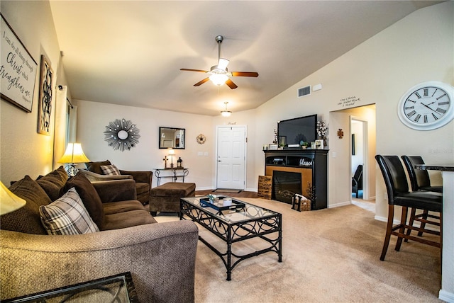 living room featuring ceiling fan, vaulted ceiling, a glass covered fireplace, baseboards, and light carpet