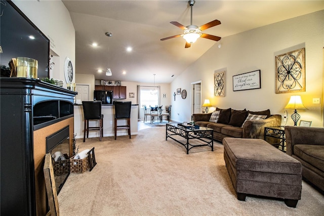 living area with vaulted ceiling, ceiling fan, light carpet, and a glass covered fireplace