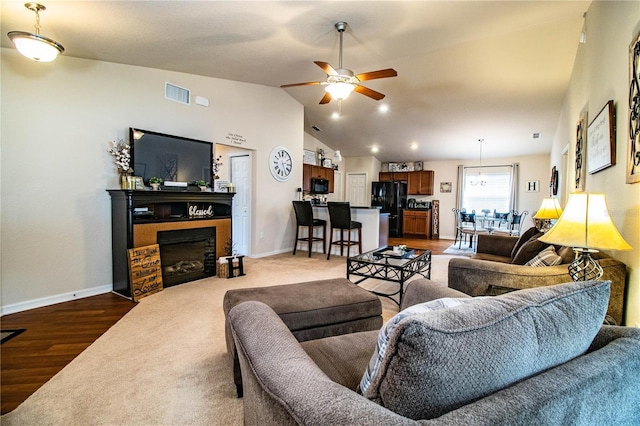 living area with a ceiling fan, baseboards, a fireplace, wood finished floors, and vaulted ceiling