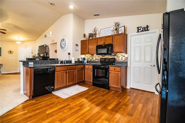kitchen with black appliances, vaulted ceiling, dark wood-style flooring, a peninsula, and brown cabinetry