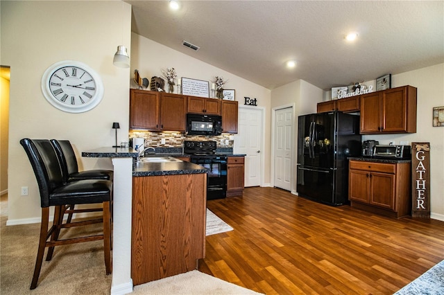 kitchen with black appliances, a peninsula, dark countertops, decorative backsplash, and a sink