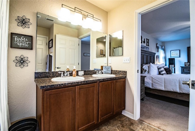 ensuite bathroom with baseboards, double vanity, and a textured wall