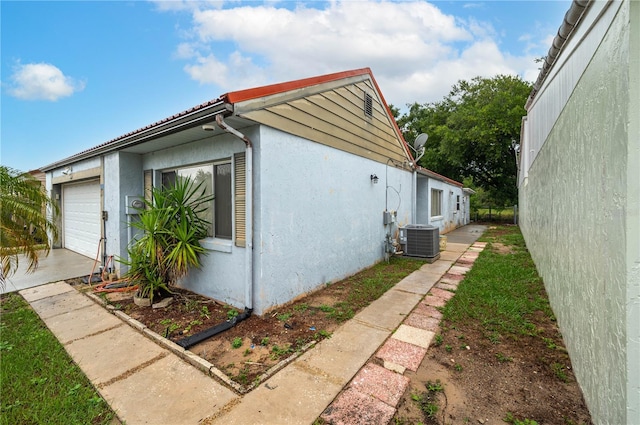 409 San Jose Dr, Winter Haven, FL 33884 - view of property exterior featuring stucco siding, central AC unit, an attached garage, and concrete driveway