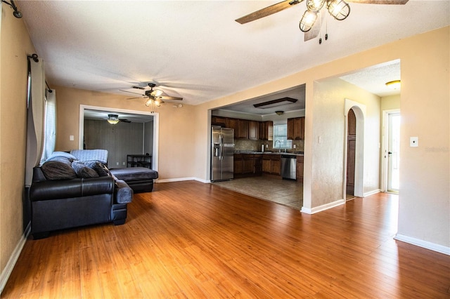living room with ceiling fan, wood finished floors, baseboards, and arched walkways