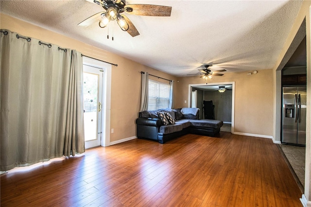 living room with a ceiling fan, a textured ceiling, baseboards, and wood-type flooring