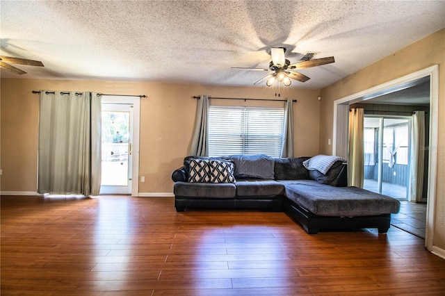 living area with a ceiling fan, a textured ceiling, dark wood-style flooring, and plenty of natural light