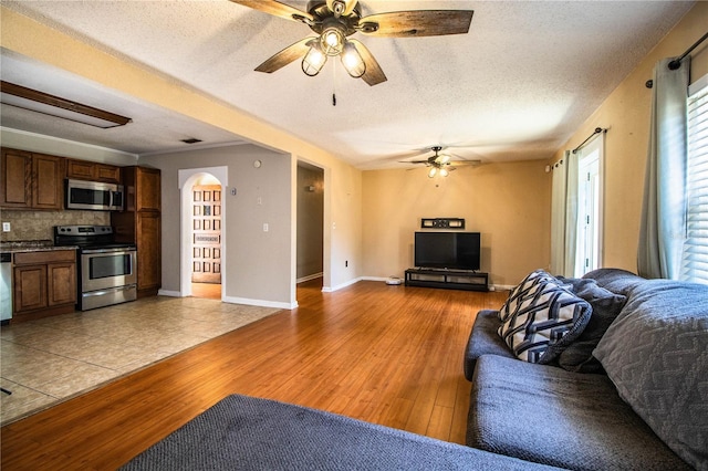 living room with a ceiling fan, light wood-type flooring, a textured ceiling, and arched walkways