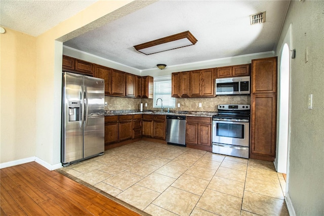 kitchen featuring stainless steel appliances, a sink, tasteful backsplash, baseboards, and a textured ceiling