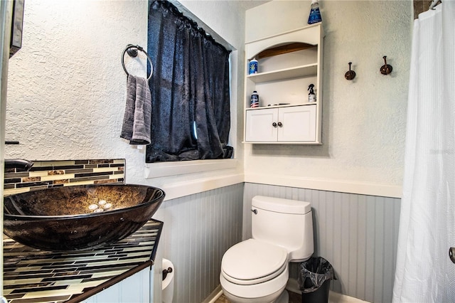 bathroom with wainscoting, toilet, vanity, and a textured wall