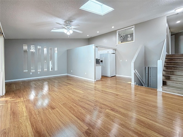 6350 92nd Pl N Unit 2206, Pinellas Park, FL 33782 - unfurnished living room with light wood-style floors, a skylight, a textured ceiling, a ceiling fan, and baseboards