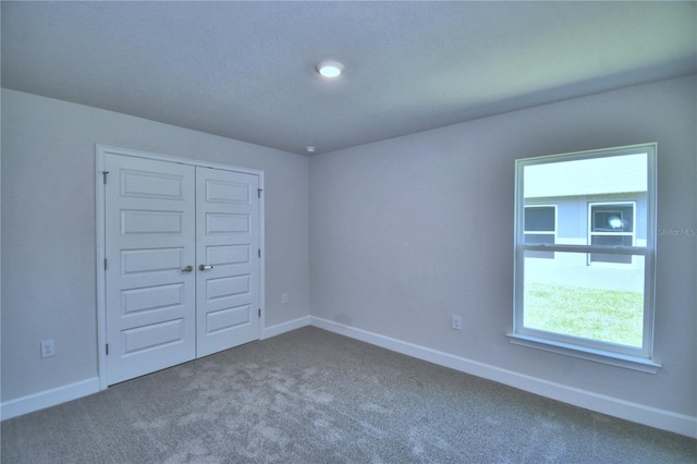 unfurnished bedroom with dark colored carpet, baseboards, and a closet
