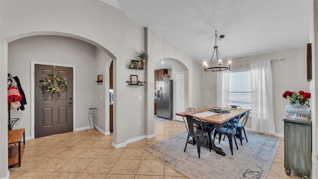 dining area featuring arched walkways, a chandelier, light tile patterned floors, baseboards, and lofted ceiling