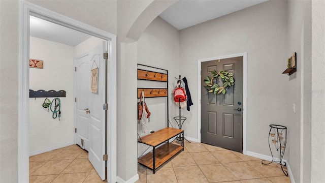 foyer entrance with light tile patterned flooring, arched walkways, and baseboards