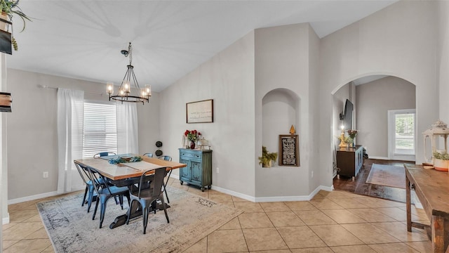 dining room with arched walkways, light tile patterned floors, a chandelier, baseboards, and high vaulted ceiling