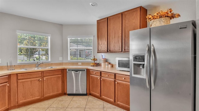 kitchen featuring appliances with stainless steel finishes, a sink, light countertops, light tile patterned floors, and brown cabinetry