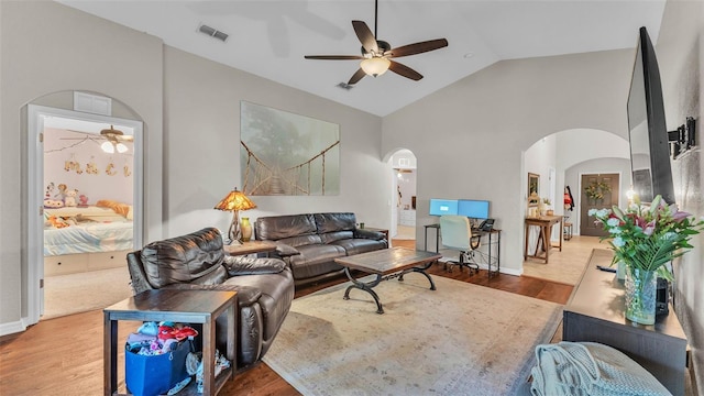 living room with arched walkways, a ceiling fan, wood finished floors, baseboards, and high vaulted ceiling