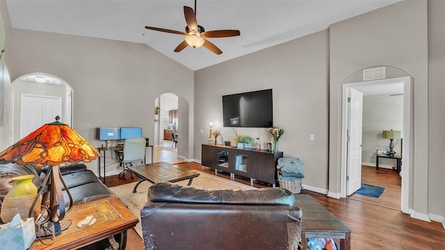 living area featuring arched walkways, a ceiling fan, vaulted ceiling, wood finished floors, and baseboards