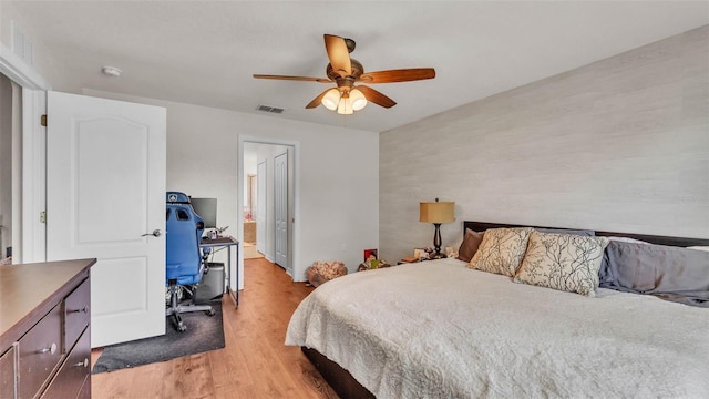bedroom with light wood-style flooring, a desk, a ceiling fan, and connected bathroom