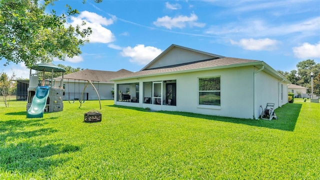 rear view of property with stucco siding, an outdoor fire pit, a sunroom, and a playground